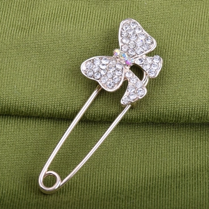 Close-up of crystal butterfly safety pin brooch with rhinestones on green fabric