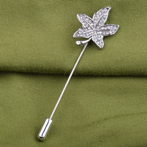 Close-up of a maple leaf brooch with crystals and pearls on green fabric