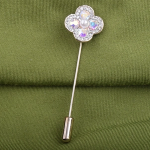 Vue macro d'une broche trèfle avec cristaux AB et perle sur tissu vert foncé
