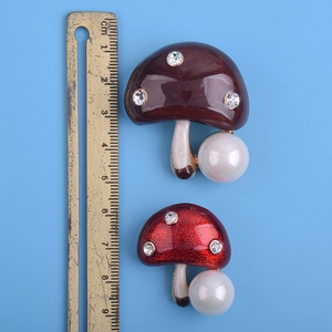 Détail de broches champignon rouges et brunes avec perles et strass sur fond bleu