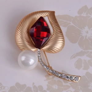 Detalle del broche de hoja en oro mate con gema roja, perla grande y brillantes blancos