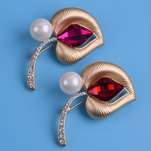 Detalle de broche de hoja dorada vintage con cristal rojo y perla blanca elegante