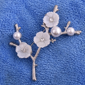 Détail macro d'une broche branche de prunier avec fleurs en nacre et perles blanches