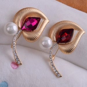 Detalle de broches de hoja dorada con cristal rojo y perla blanca sobre fondo elegante