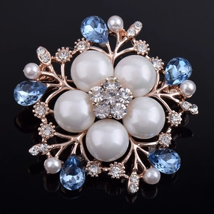 Macro d'une broche fleurie avec perles blanches, cristaux bleus et monture dorée