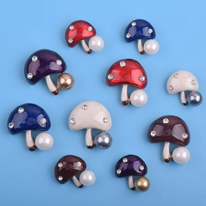 Détail de broches champignon colorées avec émail, strass et perles sur fond bleu