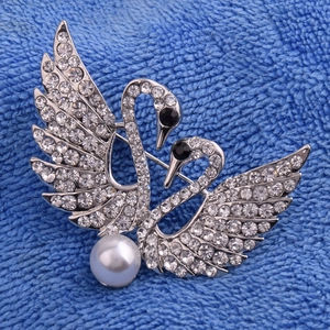 Détail macro d'une broche double cygne argentée sertie de cristaux et ornée d'une perle