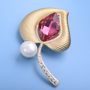 Broche étnico de hoja en oro mate con cristal rosa y perla sobre fondo azul