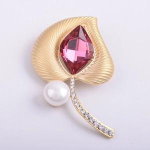 Broche de hoja étnica en oro mate con cristal rosa y perla sobre fondo blanco