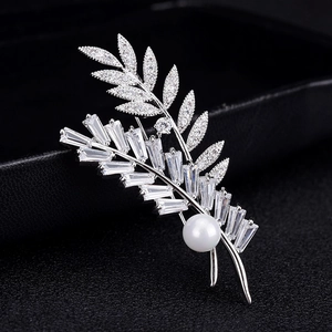 Broche élégante en forme de feuille avec zircons et perle blanche sur fond cuir