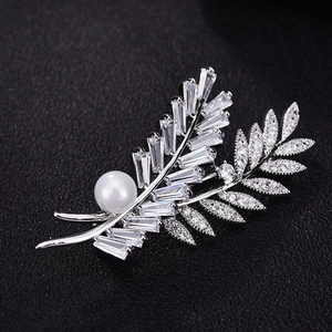 Détail macro d'une broche feuille avec cristaux baguette, micro-diamants et perle blanche ronde