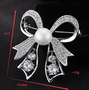 Macro shot of silver bow brooch with zircon inlay and white pearl showing dimensions