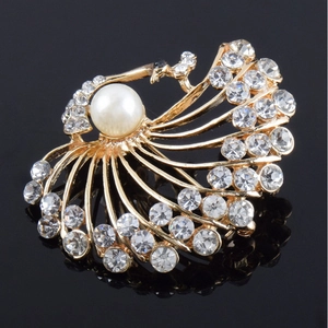 Detailed macro view of golden peacock brooch with white pearl and sparkling rhinestones