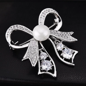 Elegant silver bow brooch with white zircon crystals and a central pearl on black leather