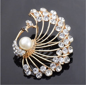 Elegant gold peacock brooch with white rhinestones and a large pearl on black surface