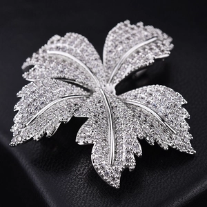 Sparkling maple leaf brooch with zircons on silver base against black leather