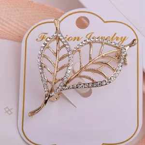 Détail de la broche feuilles dorées avec cristaux blancs et design évidé élégant