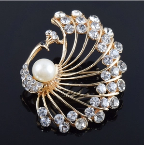 Close-up of golden peacock brooch featuring crystal feathers and a large white pearl center