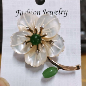 Détail d'une broche fleur avec pétales en nacre, pierre verte et placage d'or