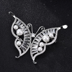 Detail of luxury silver butterfly brooch with zircon stones and white pearls on black texture
