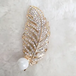 Detail der goldenen Federbrosche mit glitzernden Kristallen und einer großen weißen Perle