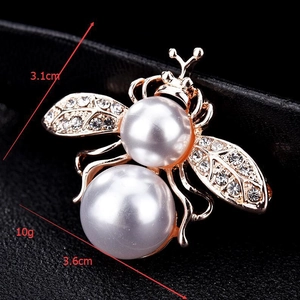 Détail macro d'une broche abeille avec perles blanches et strass mesurant 3,1cm x 3,6cm