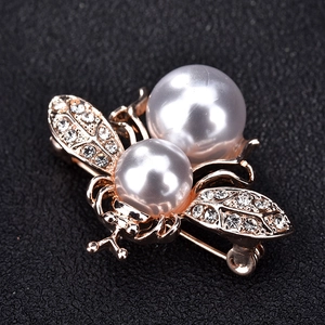 Détails d'une broche abeille dorée avec perles blanches et ailes en strass scintillants