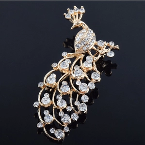 Detailed close-up of a peacock brooch with white rhinestones and golden base on a black background
