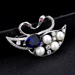 Elegant twin swan brooch with blue teardrop gemstone and pearls on dark background