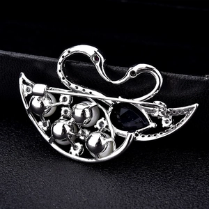 Elegant silver swan brooch with blue teardrop gemstone and pearls on black leather
