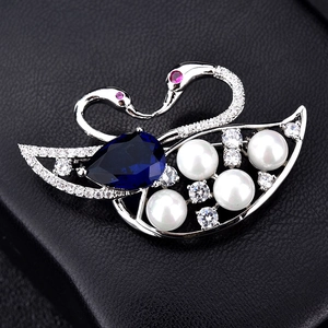 Elegant swan brooch with blue pear-shaped gemstone and pearls in a black jewelry box