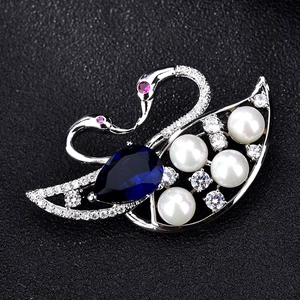 Macro detail of silver swan brooch featuring dark blue teardrop stone and white pearls