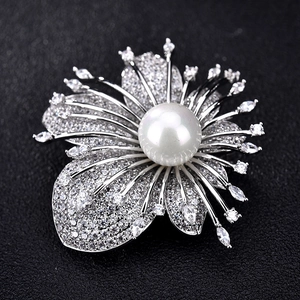 Close-up of zircon leaf brooch with central white pearl on a black textured background