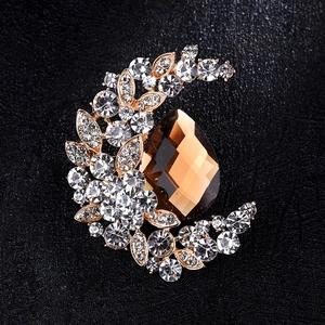 Macro detail of crescent moon brooch with amber teardrop stone and crystal pavé on black leather