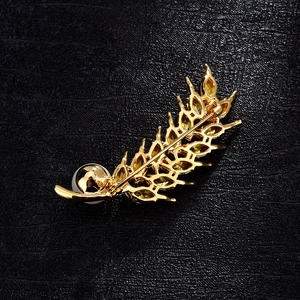 Close-up of golden wheat ear brooch with yellow zircons and white pearl on black leather