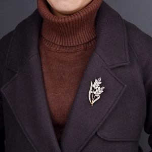 Elegant gold leaf brooch with purple and white crystals on a dark coat lapel