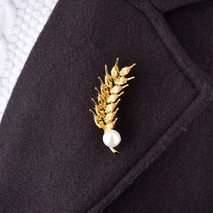 Detail of a golden wheat brooch with yellow crystals and pearl on a dark wool coat