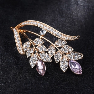 Elegant gold leaf brooch with purple crystals and white rhinestones on black background