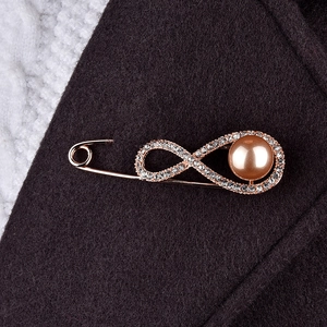 Détail d'une broche infini en or rose avec strass et perle rose sur un tissu sombre