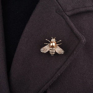 Détail de la broche abeille dorée avec perle champagne et cristaux sur col de manteau