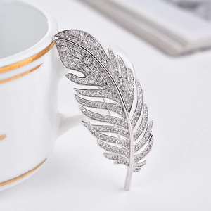 Detailed close-up of a silver feather brooch with sparkling zircons on a white surface