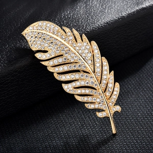 Elegant gold feather brooch with sparkling zircons on a black leather background texture