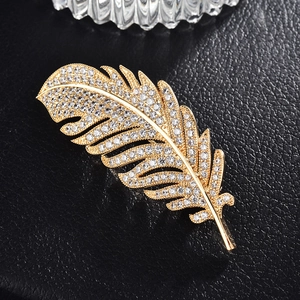Macro detail of a gold feather brooch with micro-pave zircons on black leather