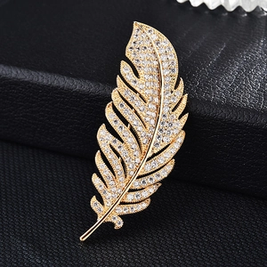 Macro shot of gold feather brooch with micro-pave zircons on a dark leather texture