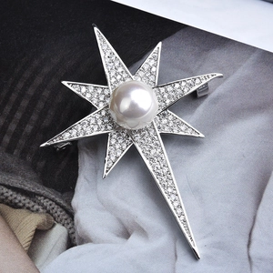 Elegant starburst brooch with a central pearl and zircon stones on a magazine background