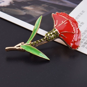 Close-up of red enamel carnation brooch with green crystal inlay on a dark background