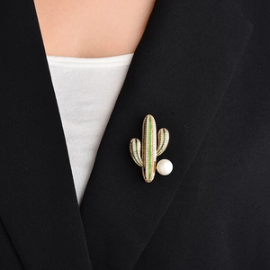 Detalle de un broche de cactus dorado con esmalte verde y una perla grande en una solapa negra