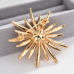 Exquisite golden sunburst brooch with radial metallic spokes on grey velvet display