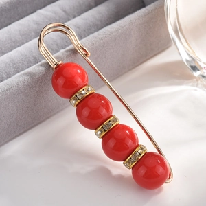 Macro shot of gold safety pin brooch with red pearls and sparkling rhinestone spacers