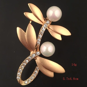 Detail view of a matte gold dragonfly brooch with white pearls and sparkling rhinestones